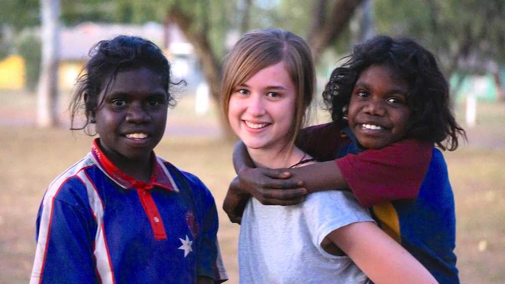 young female teacher giving piggyback to young aboriginal students on outback mission trip
